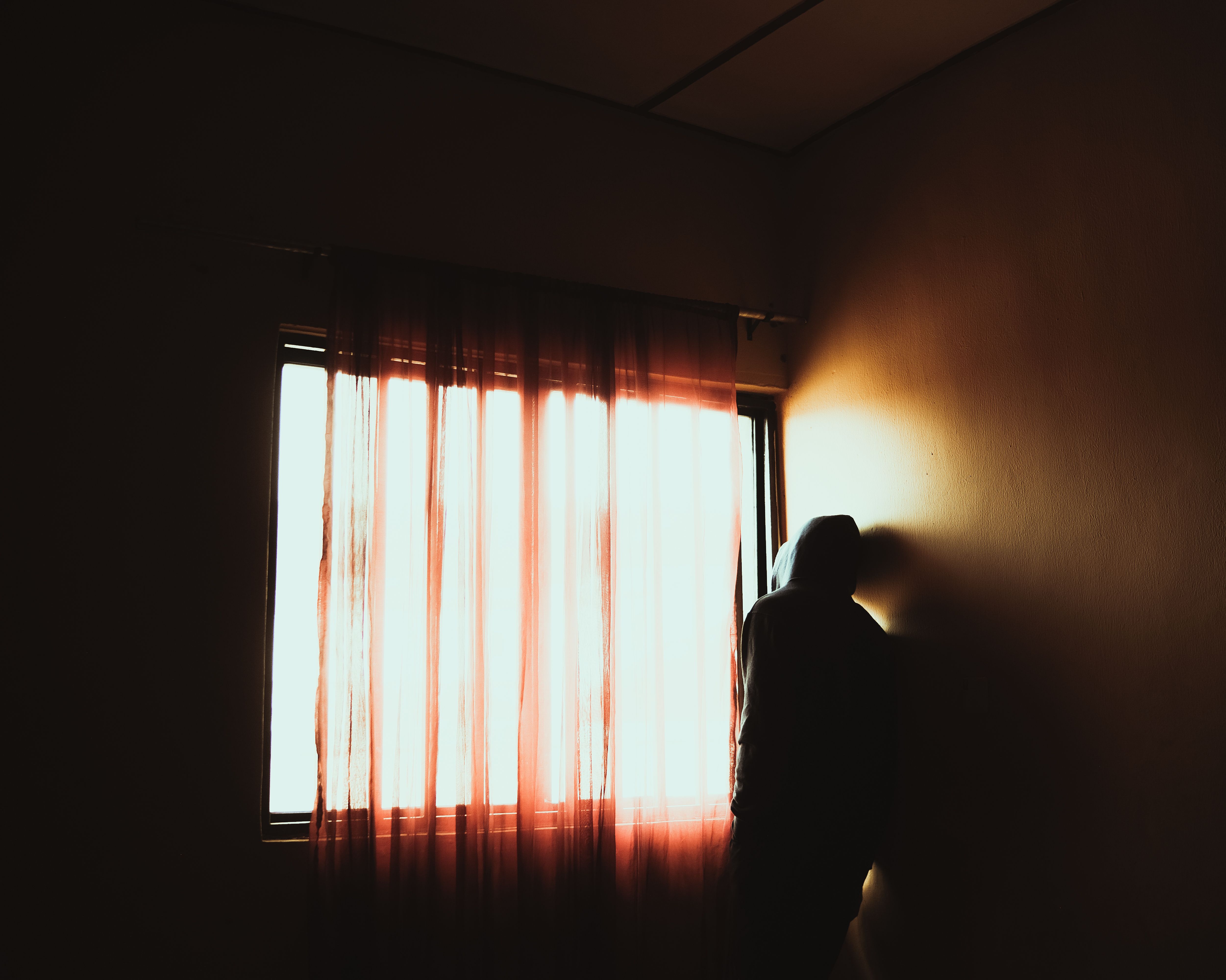 A person seated alone near a window, soft light falling across them, expression quietly contemplative — evoking the weight of unresolved moral distress.