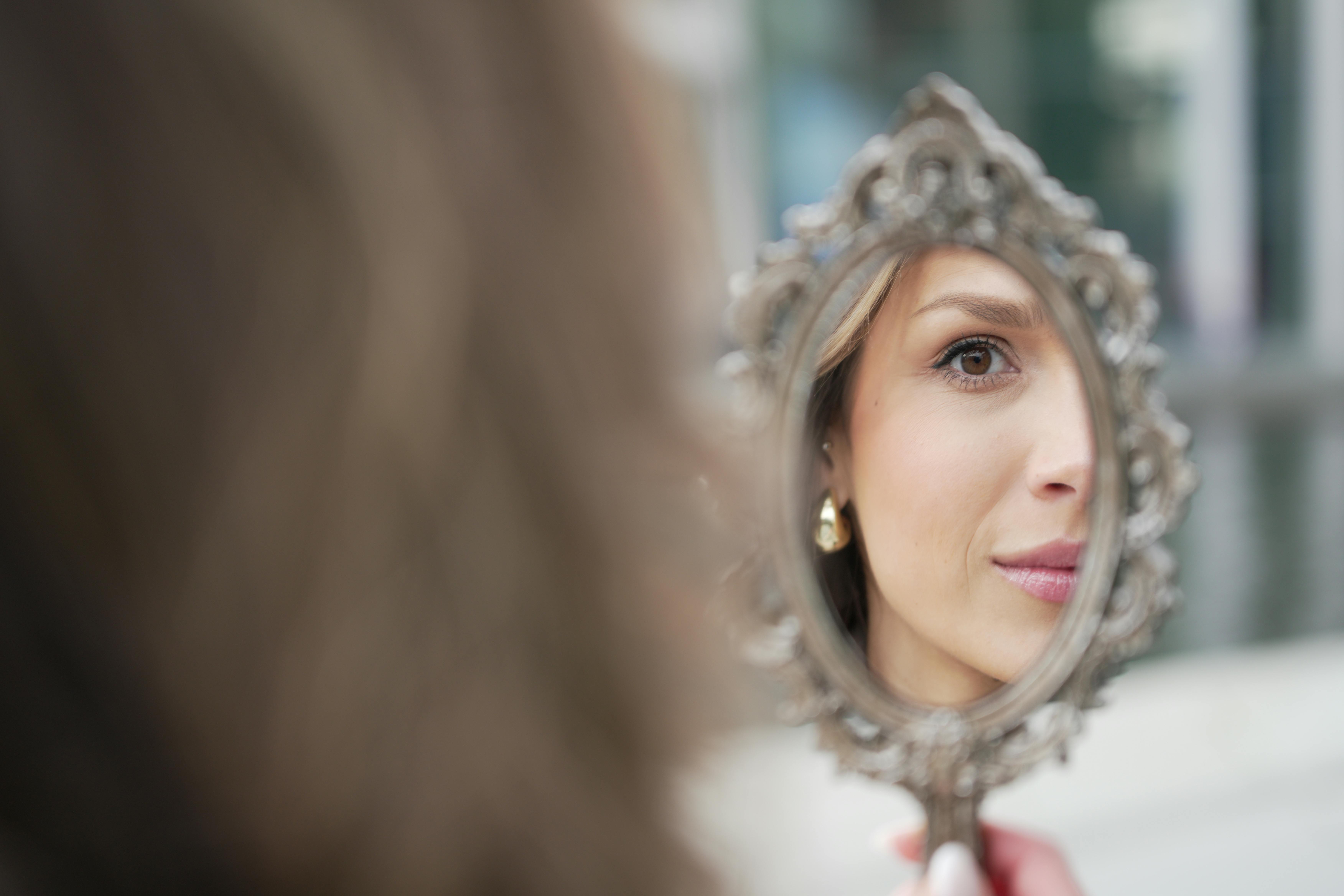 Woman looking at reflection in hand mirror, representing identity examination after late neurodivergent diagnosis