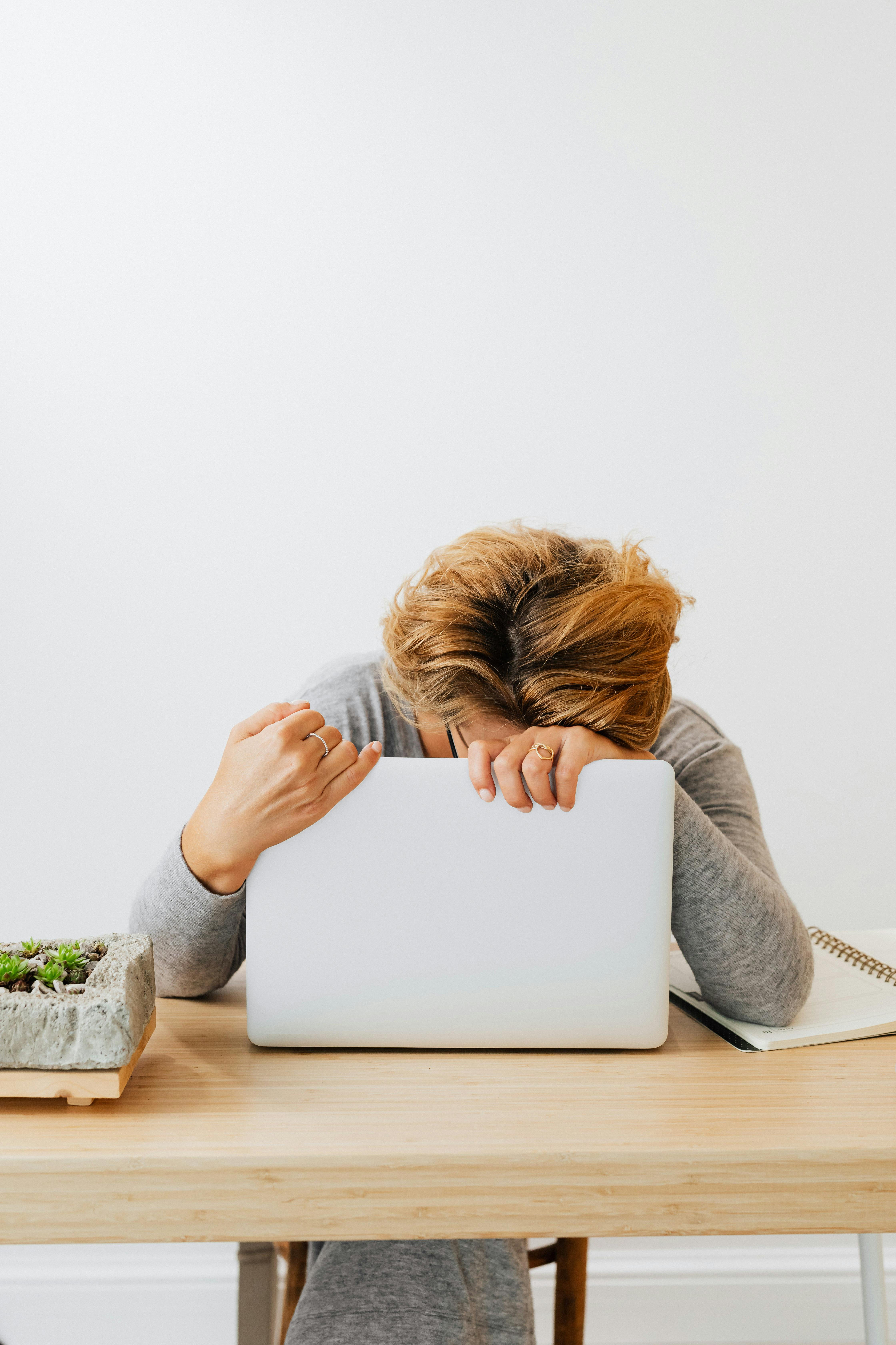 Woman with head down on laptop appearing exhausted, representing perimenopause brain fog